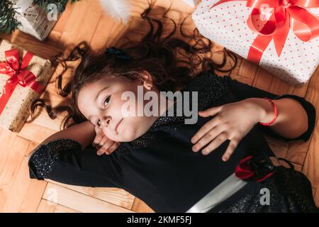 Top view of a little brunette girl lying under the Christmas tree surrounded with gift boxes Stock Photo