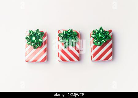 Christmas presents and new year gifts in red striped wrapping paper with green bows on white background with copy space. Stock Photo