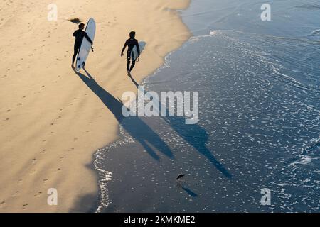 Two surfers walk along the shoreline on Oceanside City Beach in Oceanside, California. Stock Photo