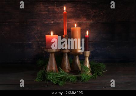 Four different candles in warm colors on wooden stands for Advent with some pine branches against a dark rustic background of wood, copy space, select Stock Photo