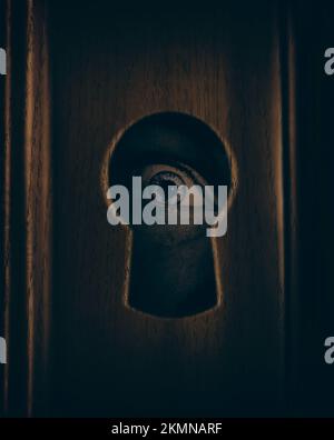 Closeup photograph of a human eye looking through a door keyhole in a spying, surveillance and security concept Stock Photo