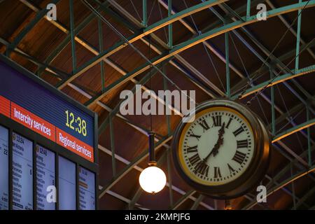 A vintage clock showing the time and the train timetable hang on the ceiling of the railway station Stock Photo