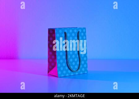 Polka dot paper bag in neon light. The concept of sales, Black Friday, cyber Monday on a blue pink background. Minimalism. Gifts, purchases, shopping. Stock Photo
