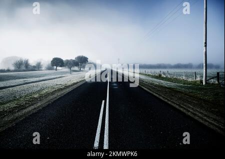Atmospheric transportation view of a cold blue winter road leading through ice caped fields of fog and frost. Saint Marys, Tasmania, Australia Stock Photo