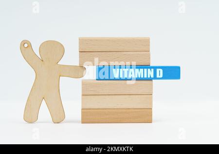 Medicine and healthcare concept. A human figurine pushes a blue wooden block labeled - VITAMIN D from a wall of blocks. Stock Photo