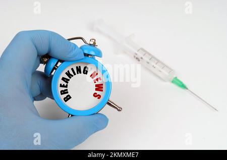 Medicine concept. There is a syringe on the table, an alarm clock in his hand with an inscription on the scoreboard - Breaking News Stock Photo