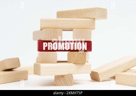 Business and finance concept. On the white surface there is a wooden destroyed tower made of planks, on the red plate there is an inscription - PROMOT Stock Photo