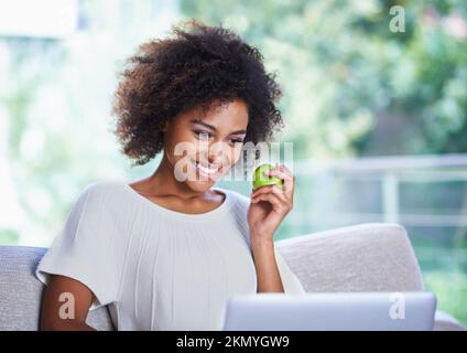 All this surfing is giving me an appetite. a young woman eating an apple and surfing the net. Stock Photo