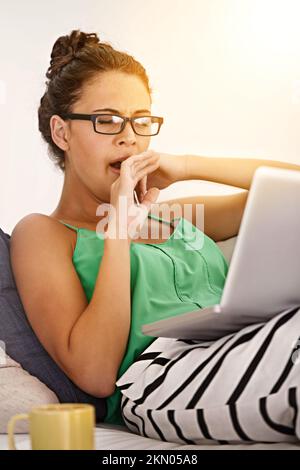 This is taking forever. a young woman yawning while using her laptop at home. Stock Photo