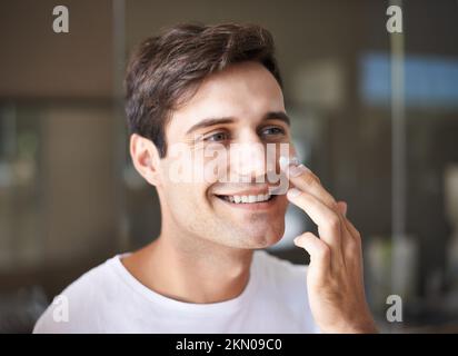 Keeping his face looking fresh and relaxed. Closeup of a young man applying lotion to his face. Stock Photo