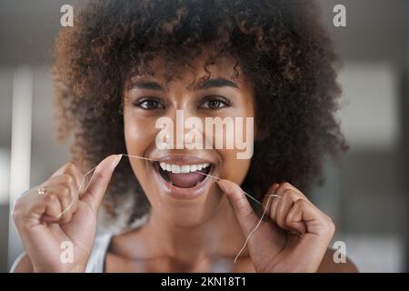 Creating the perfect smile. a young woman flossing her teeth in the mirror. Stock Photo