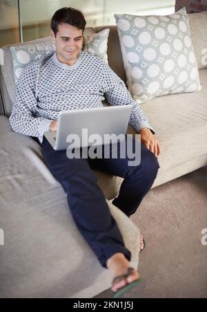 Catching up on the latest movies. a handsome young man using his laptop indoors. Stock Photo