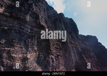 Red beach volcanic stone wall with cloudy sky Stock Photo