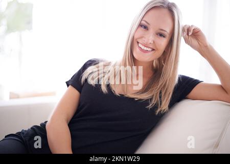 Its more than a house its a home. Portrait of a young blonde woman sitting on her sofa at home. Stock Photo
