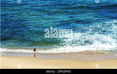 A lone older man stands at the surf edge on Newcastle Beach Stock Photo