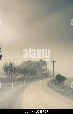 Desaturated cold blue outback Tasmania dirt road covered in thick mist. Windy paths to destinations unknown Stock Photo