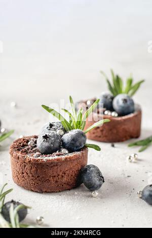 Chocolate brownies decorated with blueberries and rosemary on white textured background close up. Christmas, New Year recipe concept, menu. Text space Stock Photo