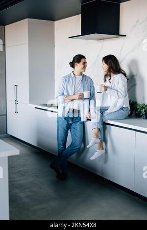 Blithesome young people talking during breakfast. Indoor photo of cheerful man drinking coffee with girlfriend. Stock Photo
