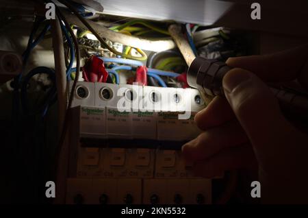 Blackout concept. Person's hand in complete darkness holding a holding a flashlight  to investigate a home fuse box during a power outage. Stock Photo