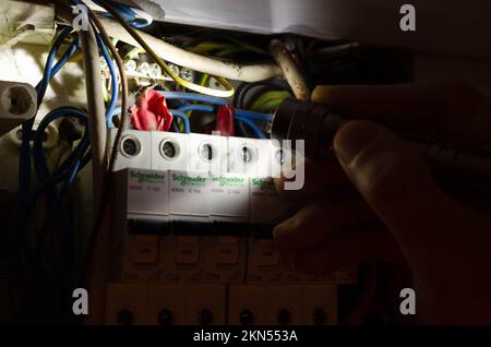 Blackout concept. Person's hand in complete darkness holding a holding a flashlight  to investigate a home fuse box during a power outage. Stock Photo