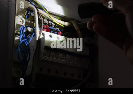 Blackout concept. Person's hand in complete darkness holding a holding a flashlight  to investigate a home fuse box during a power outage. Stock Photo