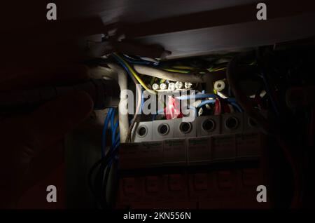 Blackout concept. Person's hand in complete darkness holding a holding a flashlight  to investigate a home fuse box during a power outage. Stock Photo