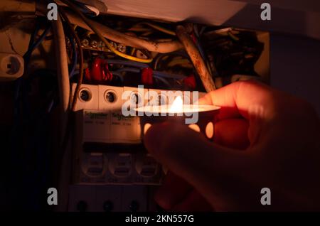 Blackout concept. Person's hand in complete darkness holding a holding a flashlight  to investigate a home fuse box during a power outage. Stock Photo