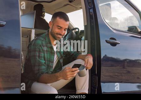 man using his mobile phone sitting on his camper Stock Photo