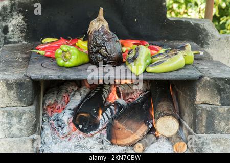 Roasting peppers and eggplant on iron plate on outdoor rustic hearth Stock Photo