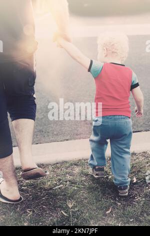 Dad holding hands while teaching son to look both ways during a road safety lesson. Sun crossing road Stock Photo