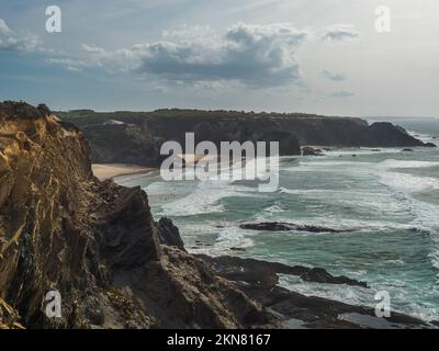 View of Praia de Odeceixe Mar beach with ocean waves, cliffs and stones, wet golden sand and green vegetation at wild Rota Vicentina coast, Odemira Stock Photo