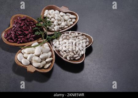 Healthy raw dried large and small white beans on a wooden dish on a stone surface, top view Stock Photo