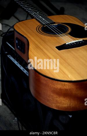 A close-up view of a natural-wood-finish acoustic-electric guitar body and preamp controls, resting on a black amplifier. Stock Photo