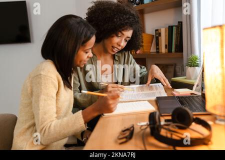Black girl writing in exercise book while doing homework with her mother at home Stock Photo