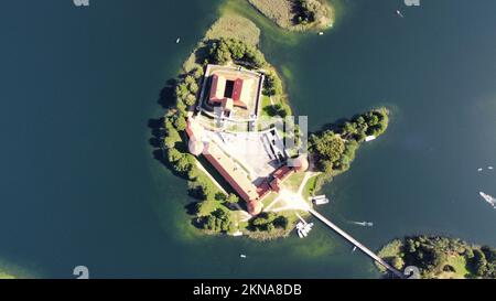 An aerial shot of Trakai Island Castle surrounded by green trees in the heart of Lake Galva