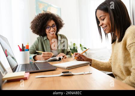 Black girl writing in exercise book while doing homework with her mother at home Stock Photo