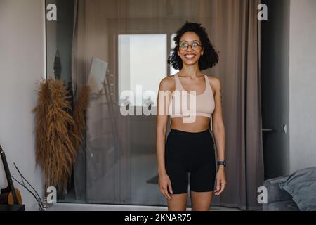 Black young woman wearing eyeglasses smiling while doing workout at home Stock Photo