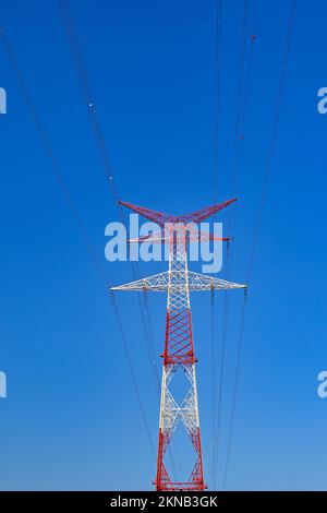 Tall pylon on an electricity supply network isolated against a deep blue sky. It is painted in red and white for visibility to aircraft. No people. Stock Photo