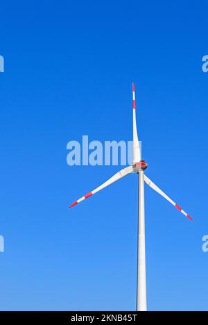 Tall wind turbine isolated against a deep blue sky. Tips of the blades are painted red and white to be visible to low flying aircraft. No people. Stock Photo