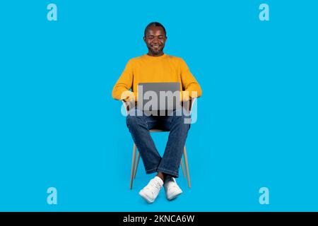 Happy african american adult man using laptop on blue Stock Photo