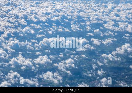 cumulus clouds on a sunny day seen from above with the ground visible below Stock Photo