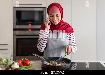 Pretty muslim woman talks on mobile phone in the kitchen Stock Photo