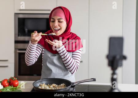 Happy Islamic Woman In Hijab Recording Video While Cooking Stock Photo