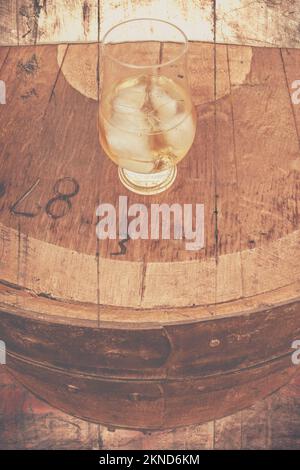 Textured close-up beverage photo on a glass of cellar brandy with ice cubes on an old rustic barrel table. High spirits Stock Photo