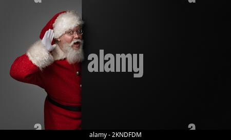 Santa Claus holding hand near ear standing with black billboard Stock Photo