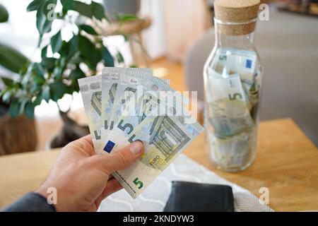 Hand holding five euro notes, saving money in a glass bottle. Stock Photo