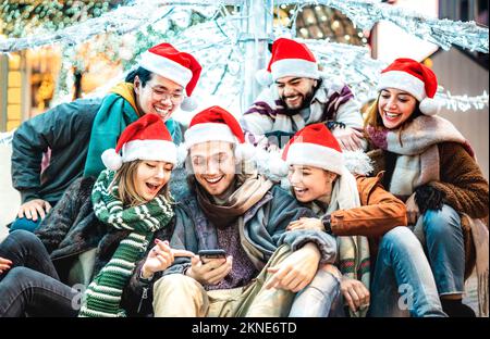 Trendy friends group wearing santa hat using mobile phone on winter Christmas holiday - Tech life style concept with happy young people Stock Photo