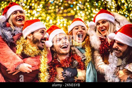 Young friends walking with santa hats at winter travel location on piggy back move - Christmas holidays life style concept with happy guys and girls Stock Photo