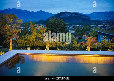 Evening view of a illuminated swimming pool with wooden walls in a beautiful garden. Stock Photo