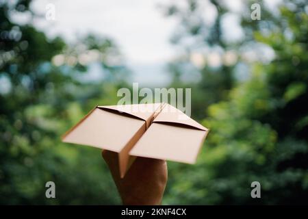 Man holding a brown paper plane in the fresh air in the forest, closeup. Space for text. Stock Photo